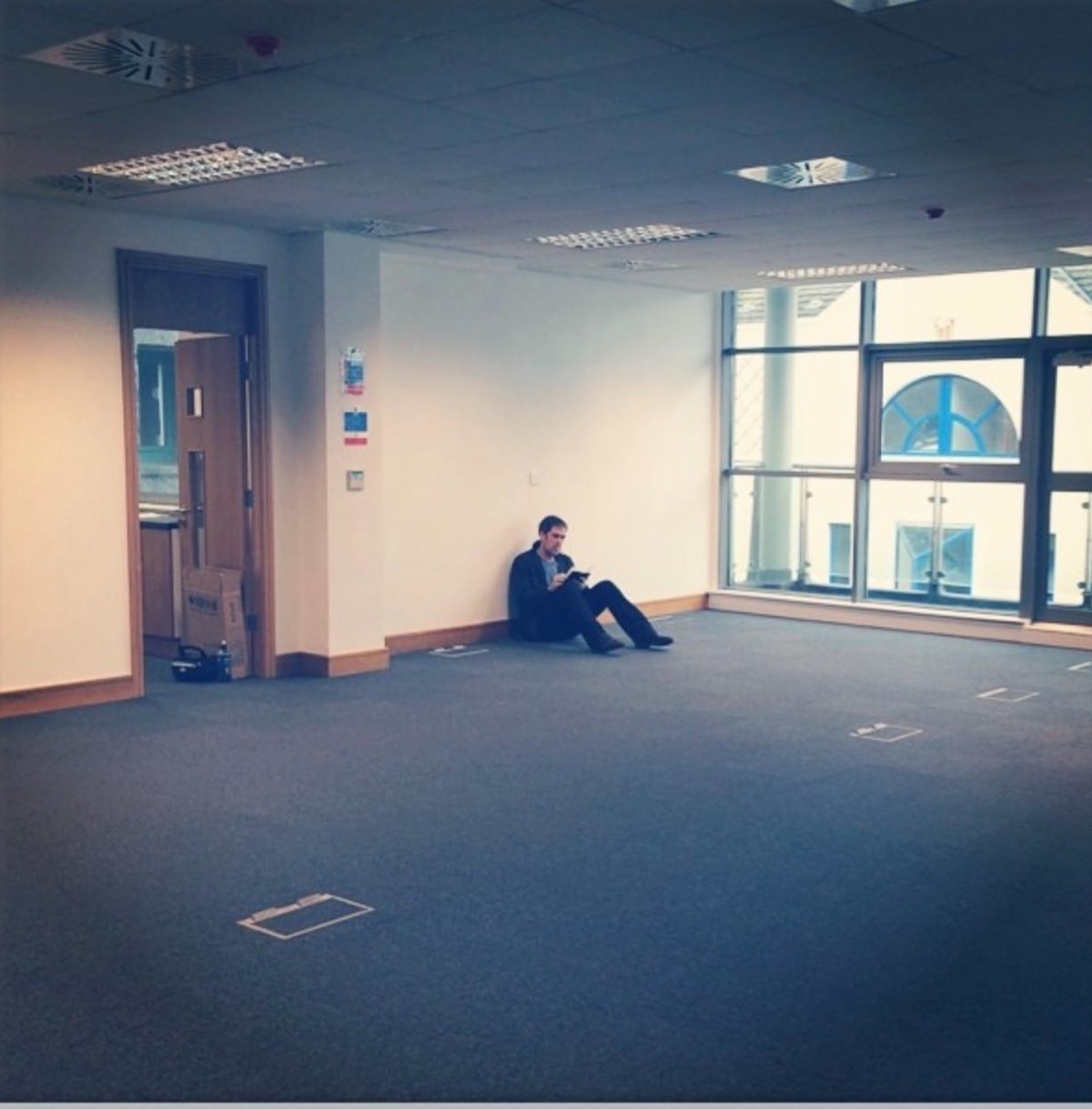 An empty office in Galway, Ireland, July 2014. Miles Kane sits on the floor against the wall with a tablet. Taped outlines on the carpet mark where the desks will go.